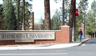Sign at the entrance of Whitworth University, with trees and campus buildings in the background.