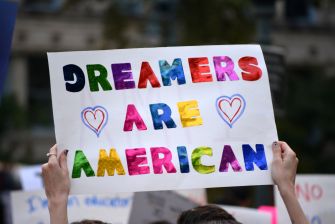 A hand holding a colorful sign that reads "DREAMERS ARE AMERICAN" at a protest.