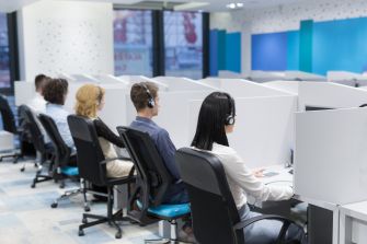 A row of customer service representatives wearing headsets, seated in cubicles at a call center.