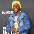 Rapper Quando Rondo smiling at a red carpet event, wearing a yellow beanie and denim jacket.