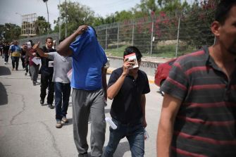 Group of individuals walking along a street, some with their faces obscured.