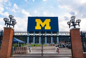 Entrance to the University of Michigan Stadium with a large blue panel bearing a yellow M logo and brick gate posts.