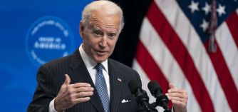 President Biden speaking at a podium with an American flag in the background.