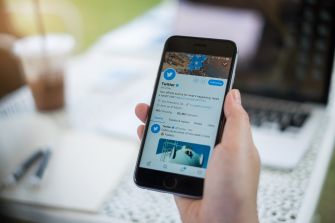 A person holding a smartphone displaying the Twitter app interface.