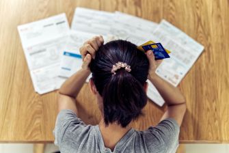 A person sitting at a table with paperwork and a credit card, looking stressed or overwhelmed by financial issues.