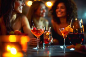 Group of friends enjoying drinks at a bar, with cocktails and a warm, festive atmosphere.
