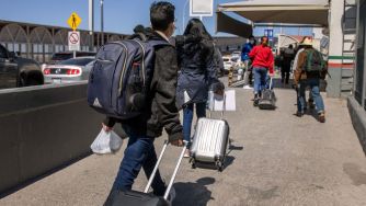 People walking with luggage towards an immigration checkpoint.