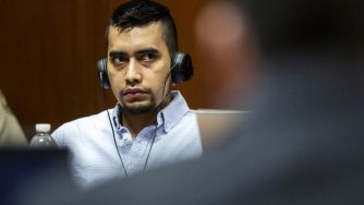 Man in a blue shirt wearing a headset sits at a table in a courtroom during a murder trial.
