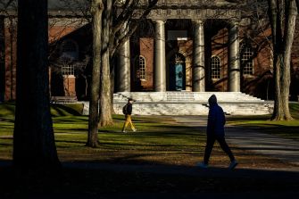 Two students walking on Harvard University's campus, with a historic building featuring columns in the background.