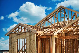 Under-construction tiny home with exposed wooden framing against a cloudy blue sky.