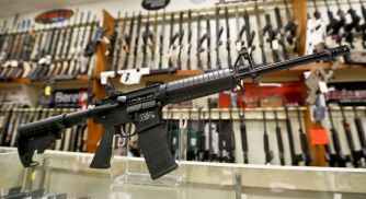 A display of firearms, including a prominent rifle in the foreground, at a gun shop.