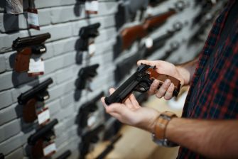 Person examining a handgun in a firearm retailer, showcasing various handguns displayed on a wall.