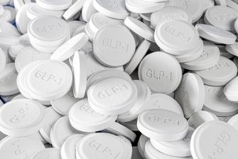 Close-up of a large pile of white round pills stamped with GLP-1.