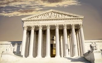 Front view of the U.S. Supreme Court building with tall columns and a sculpted pediment that reads Equal Justice Under Law, against a cloudy sky.