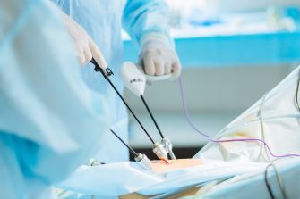 Surgeons in sterile blue gowns using laparoscopic surgical instruments in an operating room.