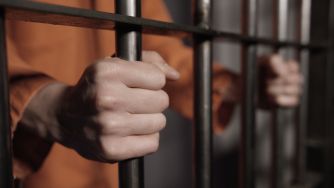 A close-up of a person's hands gripping prison bars, symbolizing incarceration.