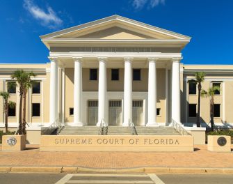Exterior of the Supreme Court of Florida, a neoclassical courthouse with tall white columns and steps, flanked by palm trees.
