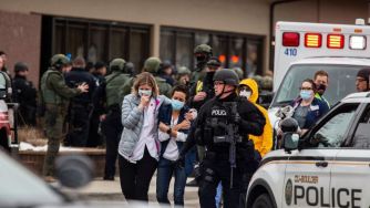 First responders assist individuals after a mass shooting incident, with police and emergency vehicles present.