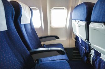 Image of airplane seats with limited legroom viewed from the aisle.