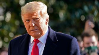 Image of Donald Trump outdoors, wearing a dark coat and a red tie.