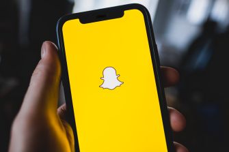 Image of a smartphone displaying the Snapchat logo on a yellow background.