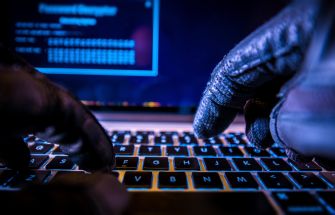 Gloved hands typing on a laptop keyboard, possibly indicating hacking activities.