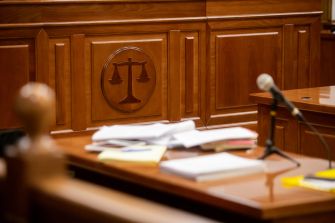 A courtroom setting featuring a wooden bench with the scales of justice emblem and a pile of documents on the table.