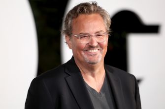 Smiling middle-aged man with gray hair and clear-frame glasses, wearing a dark blazer over a gray shirt.