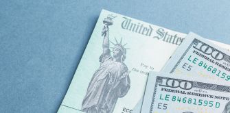 Image of a U.S. check featuring the Statue of Liberty alongside several $100 bills.