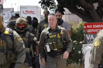 A group of law enforcement officers, including masked agents, conducting an operation in a public area in Southern California.