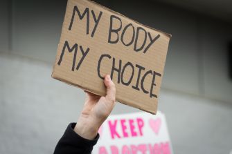 A hand holding a protest sign that reads "MY BODY MY CHOICE."