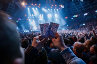 A person holding three event tickets in front of a large crowd at a concert venue.