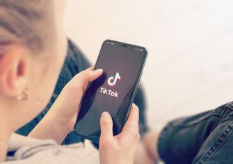 A person holding a smartphone displaying the TikTok logo on its screen.