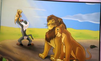 Cartoon from The Lion King showing a meerkat lifting up a cub while a lion watches on the savannah.