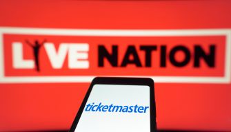 Blurred red Live Nation sign in background with a smartphone showing the Ticketmaster logo in the foreground.
