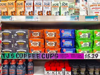 Shelf of Trader Joe’s store-brand coffee bags in various colors displayed on a grocery store shelf.