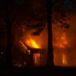 A house engulfed in flames during a fire incident at night, surrounded by trees.