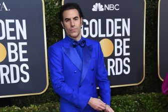 A man in a blue suit poses at an awards event, with promotional banners in the background.