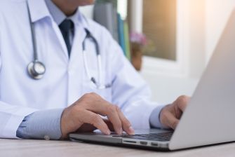 A doctor in a white coat typing on a laptop, representing the telemedicine aspect of healthcare.