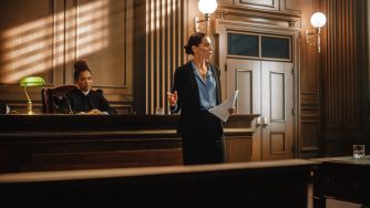 A lawyer giving a presentation in a courtroom, with a judge seated in the background.