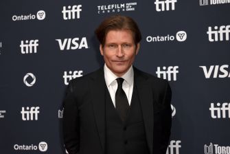 Portrait of a man in a black suit and tie standing in front of a TIFF backdrop with logos.