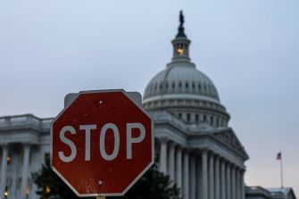 A stop sign in the foreground with the U.S. Capitol building in the background during dusk.