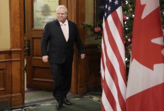 Doug Ford, Ontario Premier, walking into a room with Canadian and U.S. flags in the background.
