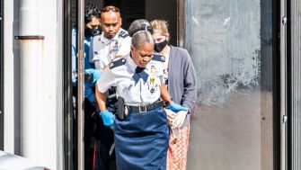 A woman in police custody is led away by officers in the Cayman Islands, following her arrest for violating COVID-19 quarantine protocols.
