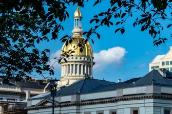 Gold-domed state capitol building framed by tree branches against a blue sky.