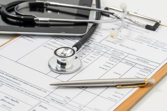 A stethoscope, pen, and medical forms on a clipboard, representing healthcare services and billing.