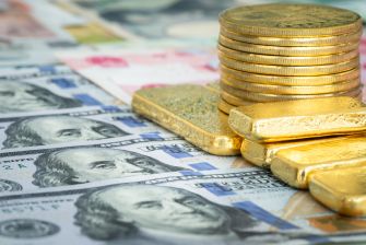 Stacks of gold bars and coins on a background of various currency notes.