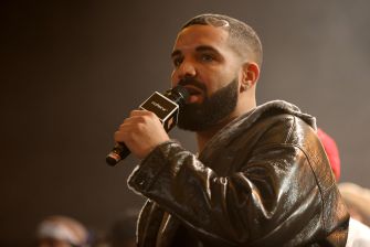 Close-up of a man with a beard and earring speaking into a microphone during an event, wearing a leather jacket.