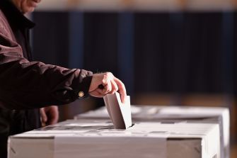 A person inserting a ballot into a ballot box.