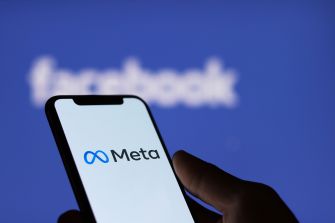 Close-up of a smartphone displaying the Meta logo against a blue, blurred background.